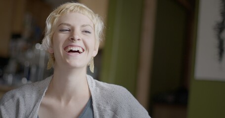 Close up of attractive young woman with short blonde hair laughing during a conversation in an...