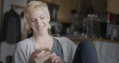 Attractive young woman laughs while using a smart phone in urban loft location. Medium close up
