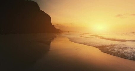 Aerial golden sunset above sandy ocean beach. Drone flying over sea waves at sun set. Tropic mountain silhouette. Beautiful light nobody wild nature landscape. Golden hour view. Hawaii tropical travel