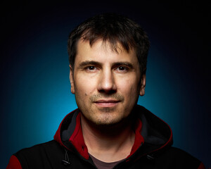 Portrait of a 42-year-old brunette man on a dark background with bright illumination