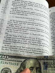 The Holy Bible in English with a tab from the $ 100 banknote showing a passage from the Gospel according to St. Matthew 6:24