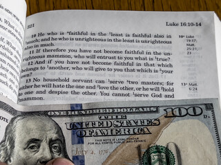 The Holy Bible in English with a tab from the US $ 100 banknote showing the passage from the Gospel...