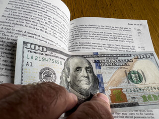 The Holy Bible in English with a tab from the US $ 100 banknote showing the passage from the Gospel...