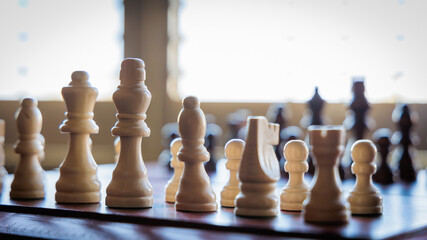Chess pieces on a board near a sunny window

