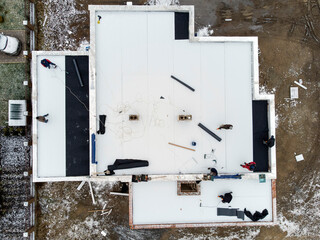 Roofing construction worker installing a flat roof. Bright blue sky in the background.