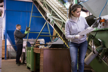 Fototapeta na wymiar Focused woman supervising sensors of machine of olive oil cold pressing on family artisanal factory