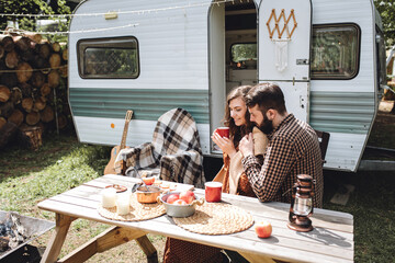 Young beautiful loving couple travelling across country in the van. Millennial man and woman in a travel camper. Cozy atmosphere, vacations vibe. Drinking tea, playing guitar