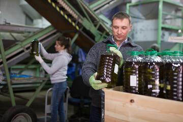 Skilled worker of artisanal olive oil factory checking and stacking plastic bottles with oil for storage