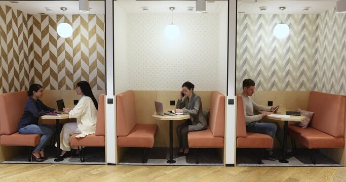 Four businesspeople working in coworking with partitions. Businesswoman make business call, two women discuss common task during meeting while businessman using digital tablet. Workflow, modern tech