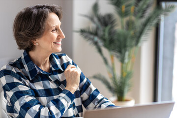 Happy successful elderly business woman sitting in modern office looking away and smiling. Portrait of a confident aged female entrepreneur