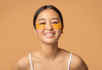 Young Asian woman with patches rejuvenation skin care on a beige background looks at the camera and smiles friendly. Healthy lifestyle