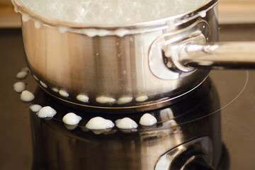 Milk porridge poured out during boiling from under the lid of the pan onto an electric induction stove