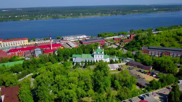 Aerial view of a village located by the river shore. Clip. Flying above summer green nature and buildings.