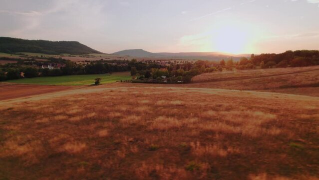 Aer ial view of a German village surrounded by meadows, farmland and forest at sunset in Germany.