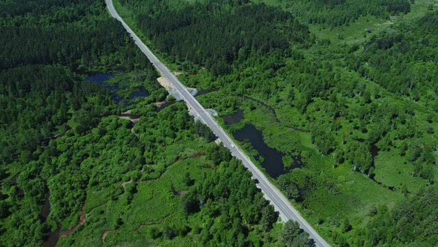 4k Top view of cars drive along road in green countryside irrl. Aerial shot of transport travels on highway along waters and green vegetation on summer day. Amazing picture from drone of