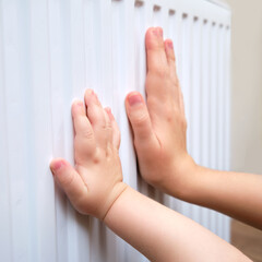 Woman mother and baby holding on to the radiator, child and adult hand on the heating system...