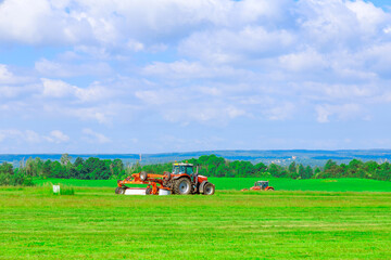 Two red tractors with a large mower in a field under a blue sky mow the grass. Haymaking, silage...