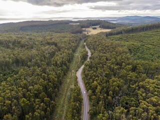 Fototapeta premium Aerial view of a highway road between forest trees in Tasmania, Australia with sunset sky