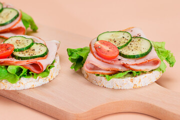 Light Breakfast. Quick and Healthy Sandwiches. Rice Cakes with Ham, Tomato, Fresh Cucumber and Green Salad on Wooden Cutting Board. Beige Background