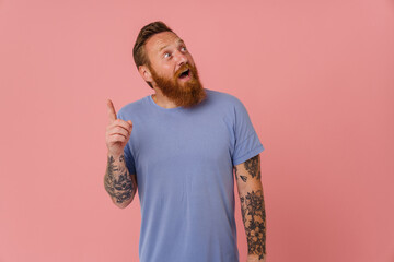 Adult redhead bearded tattooed enthusiastic man in t-shirt looking aside