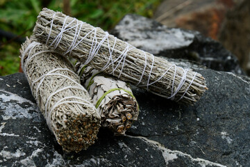 An image of three neatly stacked sage smudge stick rest on a grey stone. 