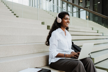 Young indian woman in headphones working with laptop outdoors