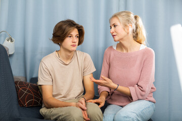 Portrait of troubled teen boy sitting at home while his mother scolding him. Family conflicts concept..