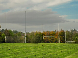 Training pitch for Irish National sport camogie, hurling, rugby and Gaelic football with tall goal posts and freshly cut grass. Nobody. Cloudy sky. Popular activity.