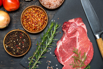Fresh meat, salt, pepper, herbs and spices with vegetables on dark table. View from above.