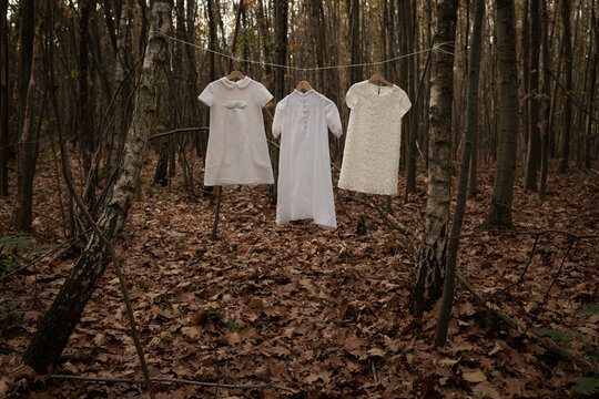 three white childrens dresses hanging on line in woods