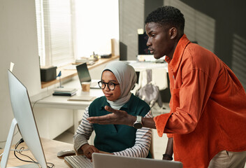 Young confident businessman consulting with Muslim female colleague during presentation of online...