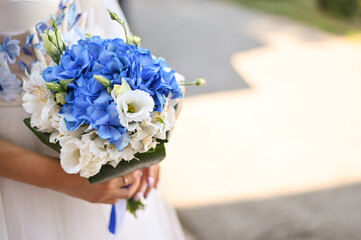 A wedding bouquet in white and blue tones in the hands of the bride. Selective focus. With free space for labels