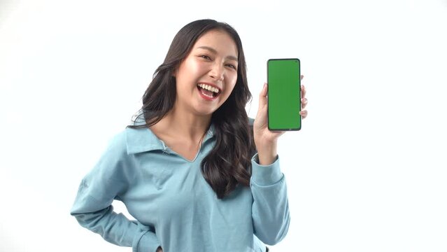 Excited surprised Asian woman showing green screen mobile phone for shopping online on white background. Enjoy girl blow a kiss presenting empty touchscreen on smartphone copy space.Technology concept