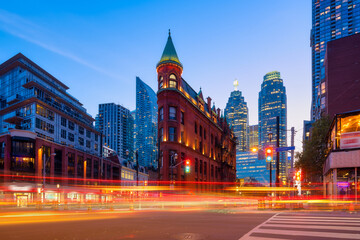 Canada, Toronto. The famous Gooderham building and the skyscrapers in the background. View of the city in the evening. Blurring traffic lights. Modern and ancient architecture. Night city.