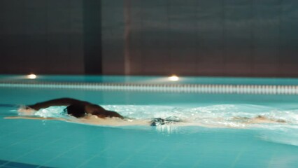 Professional swimmer man dives into the water in the pool at night