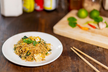 Fried noodles with eggs and basil are placed on an old wooden table.