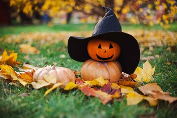 orange pumpkin snowman in black witch hat on grass and yellow leaves in fall for halloween.