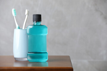 Bottle of mouthwash and toothbrushes on wooden table, space for text