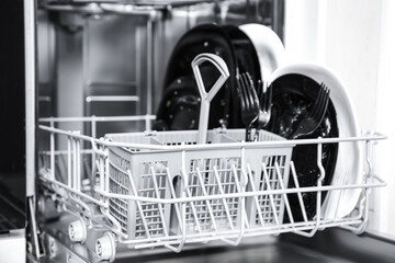 Open dishwasher with dirty tableware in kitchen, closeup