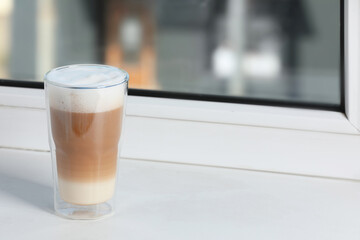 Glass with latte on white window sill. Space for text