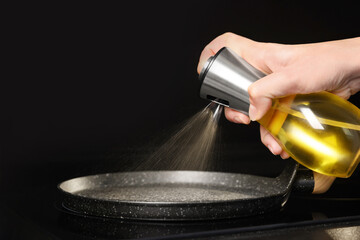 Woman spraying cooking oil onto frying pan on stove, closeup