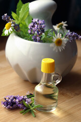 Obraz na płótnie Canvas Bottle of natural lavender essential oil near mortar with flowers on wooden table