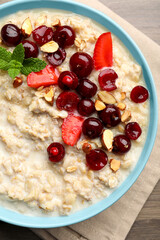 Bowl of oatmeal porridge served with berries on wooden table, top view