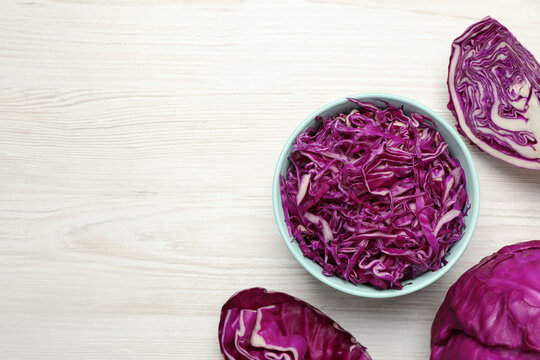 Tasty fresh shredded red cabbage in bowl on white wooden table, flat lay. Space for text