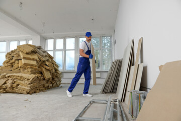 Construction worker carrying used drywall in room prepared for renovation
