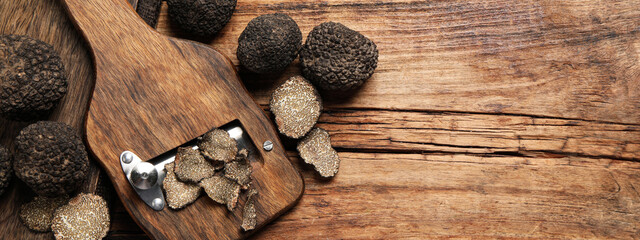 Shaver with whole and sliced black truffles on wooden table, flat lay with space for text. Banner design
