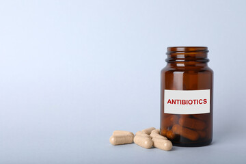 Bottle with antibiotic pills on light grey background, space for text