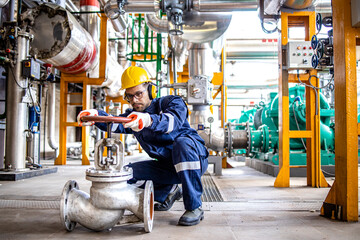 Hardworking industrial technician inspecting high pressure valve inside refinery plant.