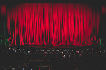 Stage with velvet red curtain in theater cinema, empty old-fashioned elegant theatre wooden stage with red cloth drapes curtains before the concert show with audience arriving, dramatic lighting