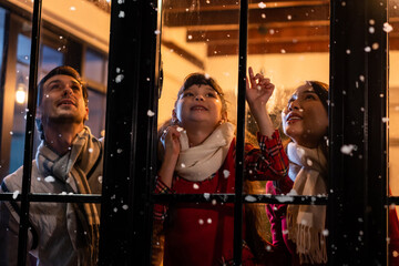 Adorable child looking at the window and first snow flakes with family.